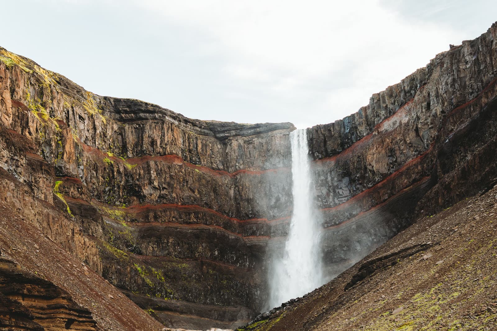 Hengifoss fällt vor roten Gesteinsschichten in ein weites Tal