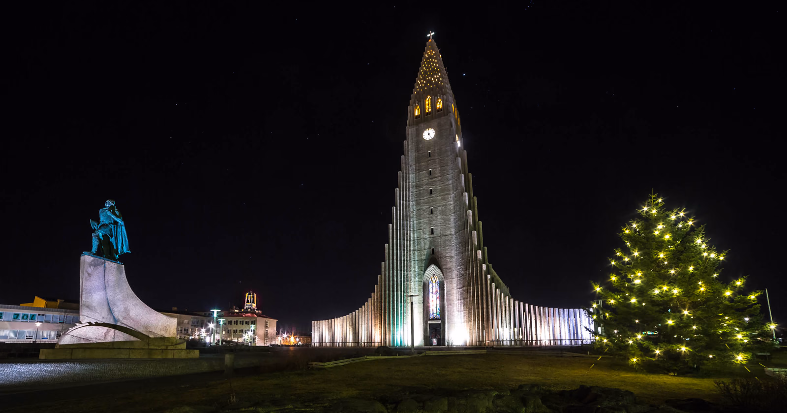 Die Hallgrímskirkja in Reykjavík bei Nacht mit Leifur-Eiríksson-Statue und beleuchtetem Weihnachtsbaum