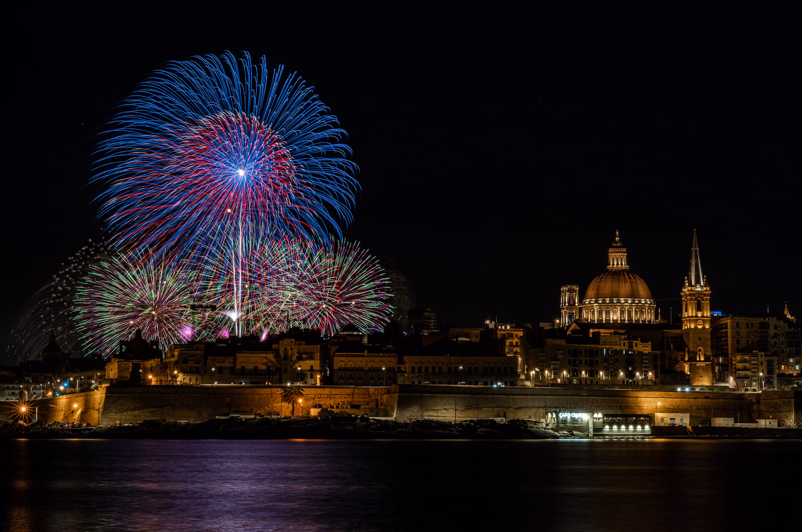 Feuerwerk über der nächtlichen Skyline von Valletta mit Kirchenkuppel, Kirchturm und Stadtmauern am Wasser