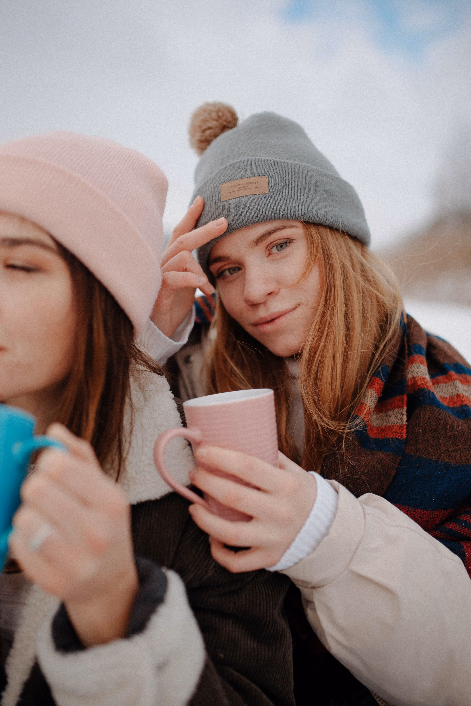 Zwei Freundinnen in Winterkleidung halten Becher mit warmen Getränken.