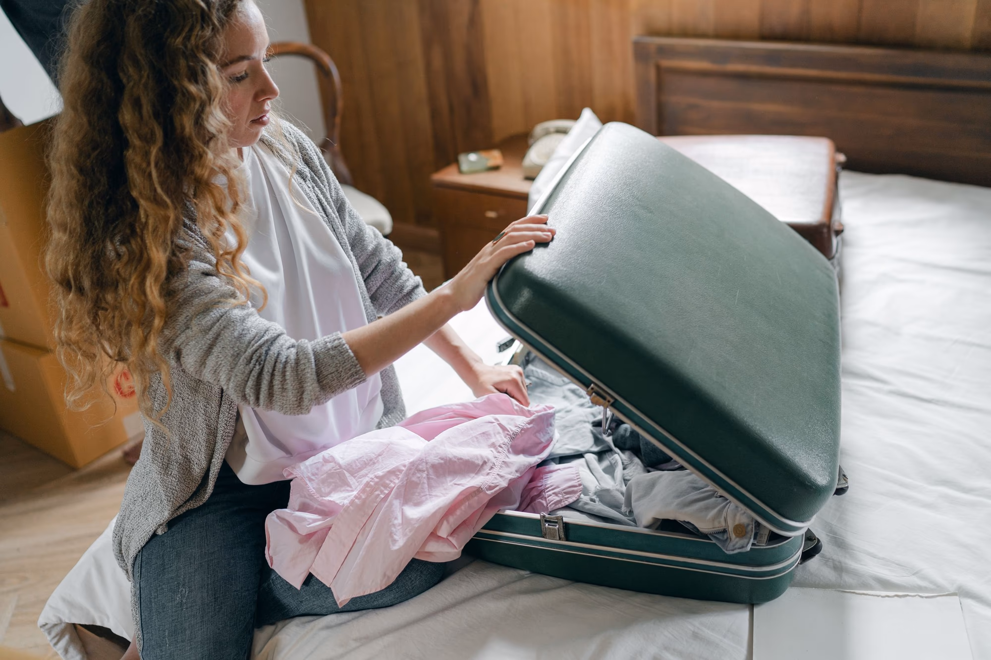Reisende packt Kleidung in einen geöffneten Koffer auf einem Bett