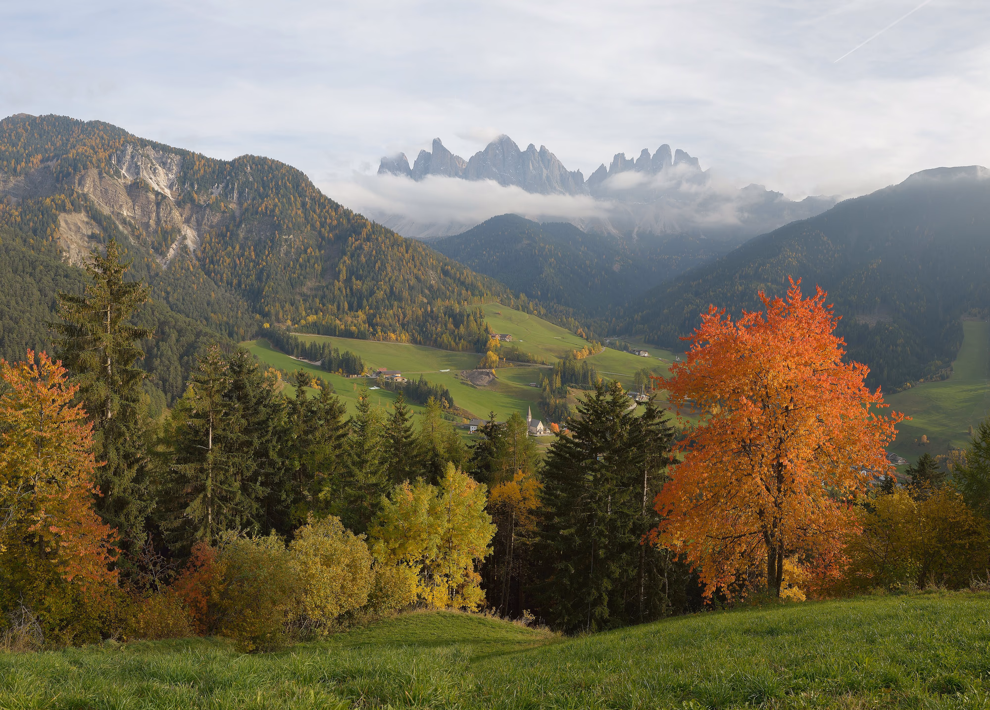 Herbstliches Villnöss mit bunten Bäumen und den Gipfeln der Geislergruppe